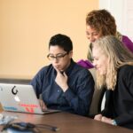 A group of people hovering over a computer learning about accounting for IT companies